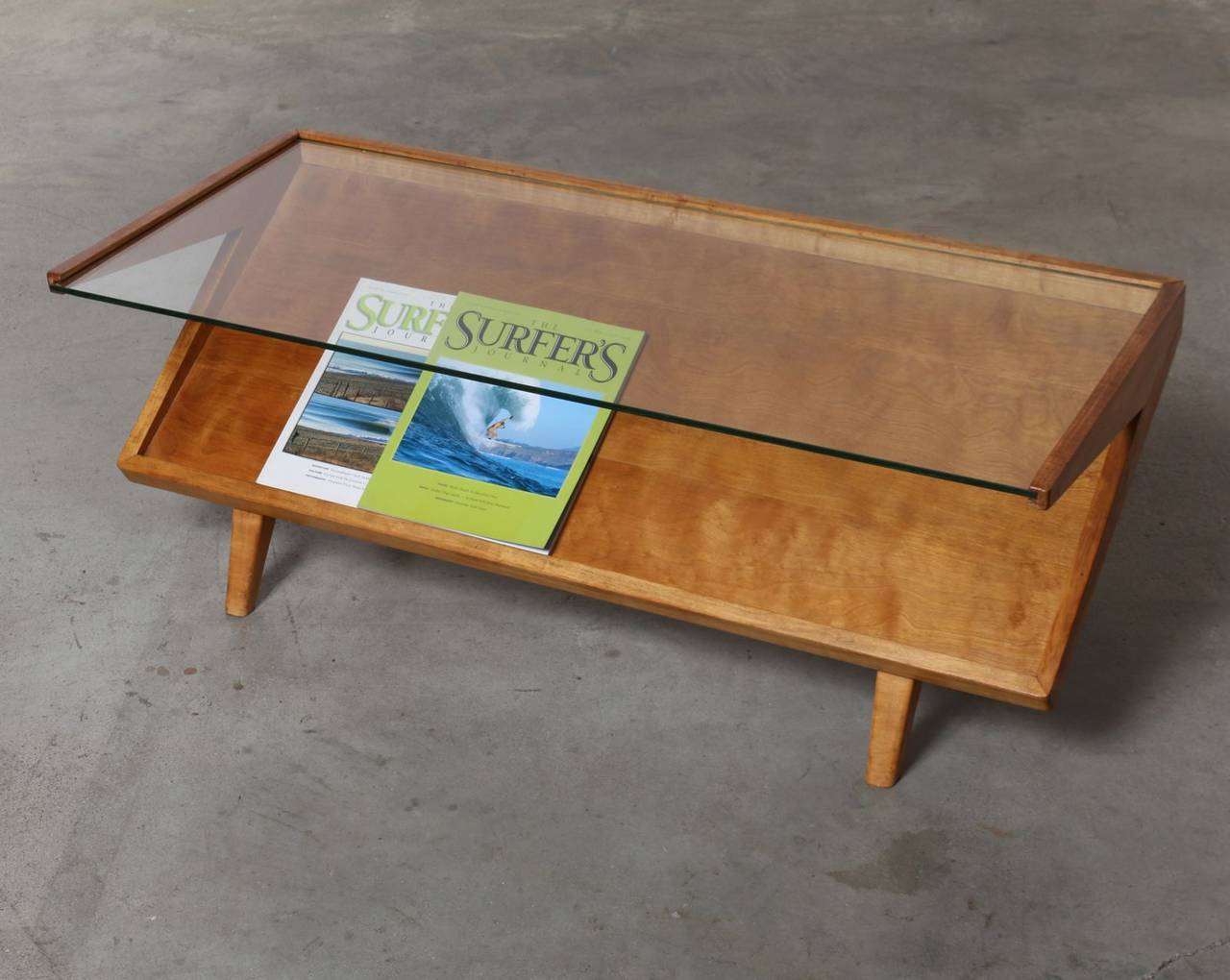 Designed by John Keal for Brown Saltman in the 1950's this sleek and shapely mid century coffee table allows viewable storage of magazines, newspapers or your favorite books below a glass top.  Boomerang shaped sides add wonderful interest and