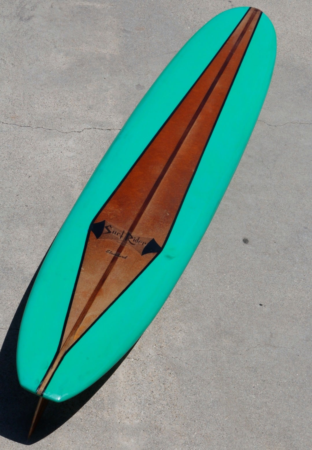 This early 1960s Surf Rider surfboard has been restored to its original luster without losing the authenticity or sensibility of its age. Teal green deck and vibrant acid splash bottom are accented by the all original natural center strip, logo,