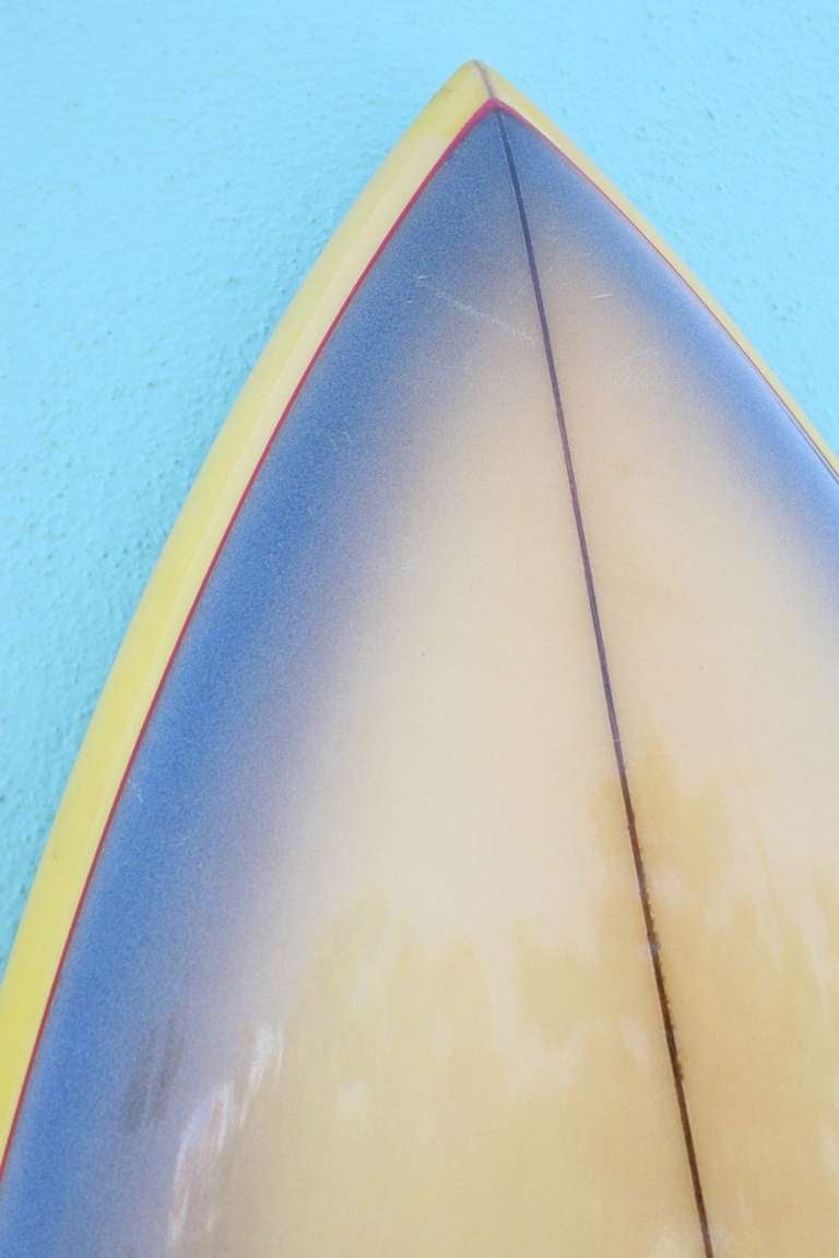 Unrestored, forty years old and outstanding. The sensibility of this surfboard warms the heart.  The balance of color, most notably the subtle interplay of yellow shades merging into purples, accented by a red pinstripe, is what first catches the