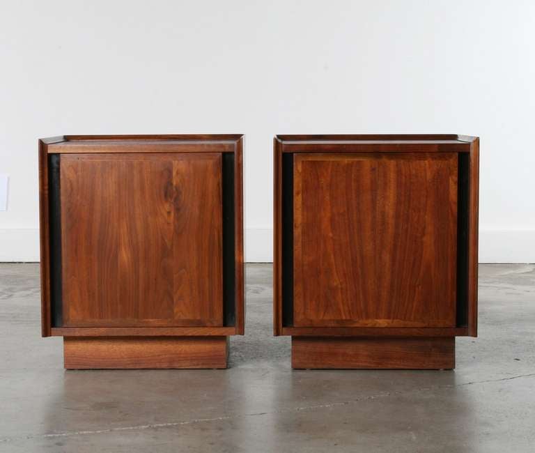 Pair of walnut nightstands by John Kapel for Glenn of California circa 1950's.  

These nightstands feature beautifully grained walnut wood.
The door on the front of the nightstands swings open to reveal a striking white drawer shadowed by black
