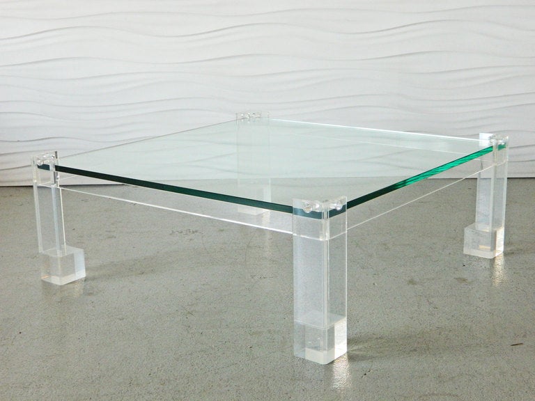 This large, low lucite and glass coffee table features a thick glass top which is held in place by lucite pegs. The base has solid lucite block feet. Custom made in the 1970s.