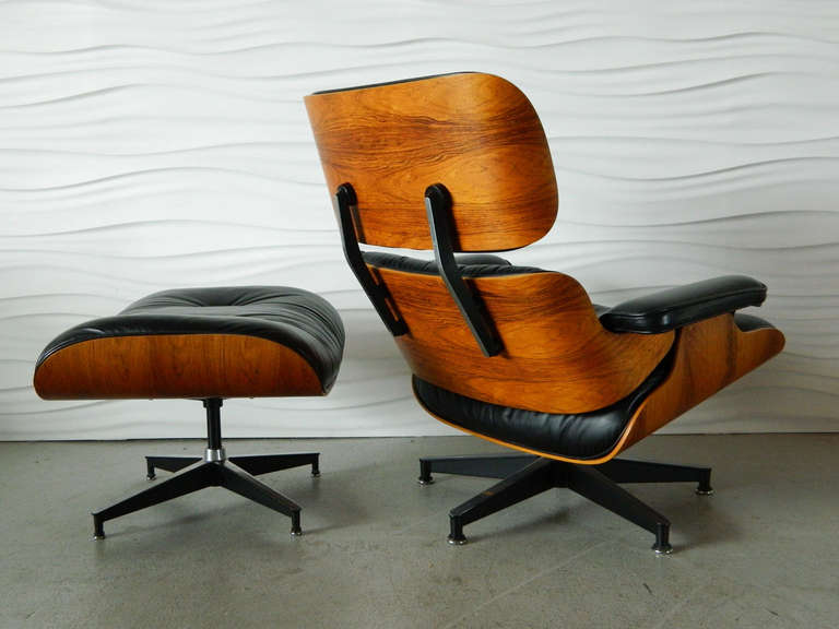 This Charles Eames 670 lounger and 671 ottoman was manufactured by Herman Miller in 1987. The shell is made of rosewood veneer and the black leather cushions are foam-filled.