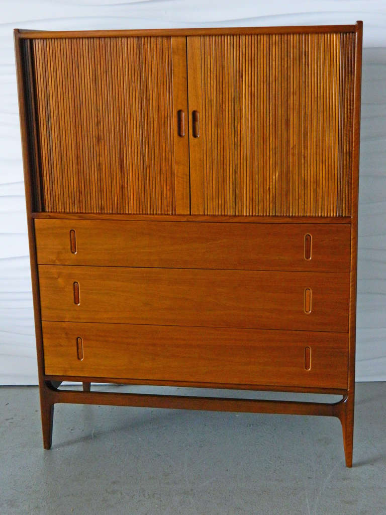 This Glenn of California chest is made of walnut and has a tambour door that conceals three movable open shelves and a vanity mirror as well as three drawers.