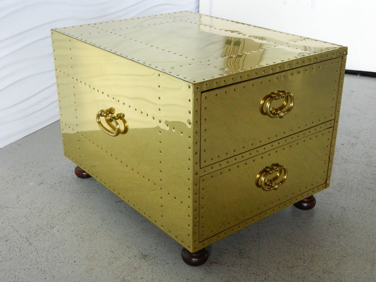 This Sarreid brass chest/trunk sits upon bun feet and has a nail head design throughout. Two drawers make it a perfect option as a stylish side table with storage.