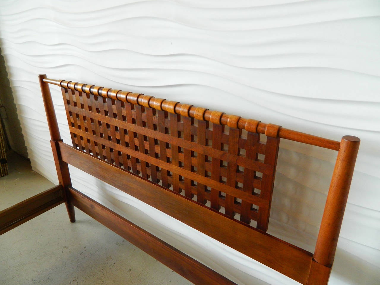This handsome American modern double bed frame has a lattice-style headboard. The turned wood top rail gives the appearance of a wrapped edge. The bed includes a headboard, footboard, two metal side rails and four wooden slats.
