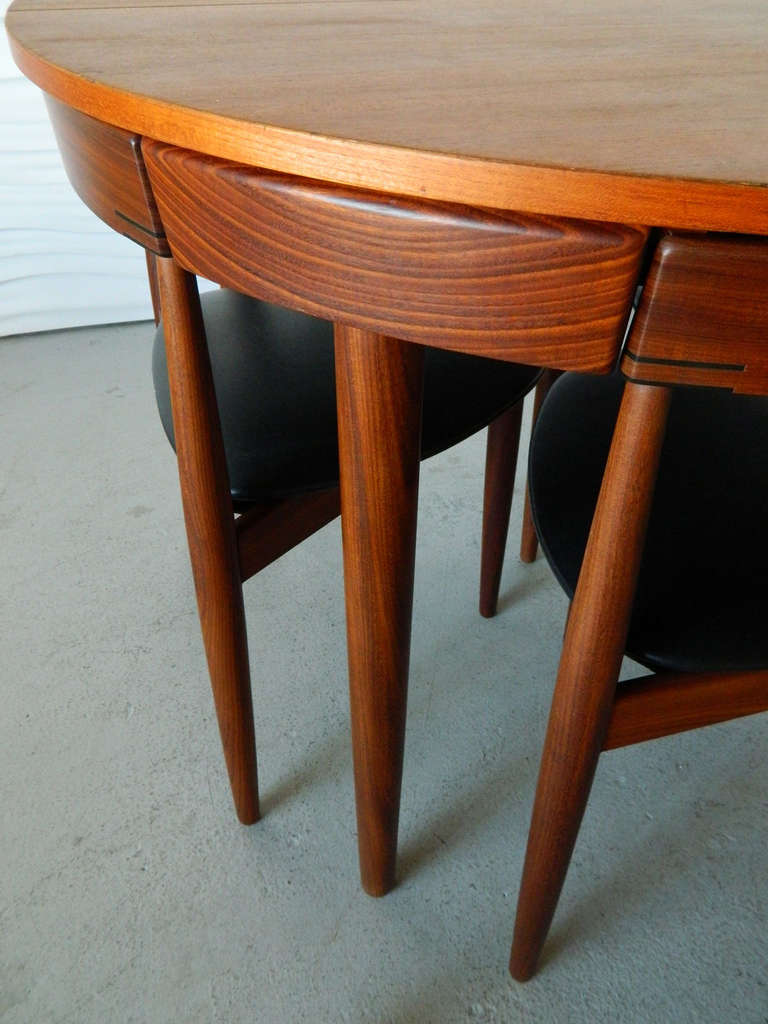 Designed by Danish designer Hans Olsen for Frem Rojle, this petite, round teak table has a self-storing leaf and four three-legged chairs which fit into the apron of the table. Chairs are covered in their original black vinyl.

Table expands to an