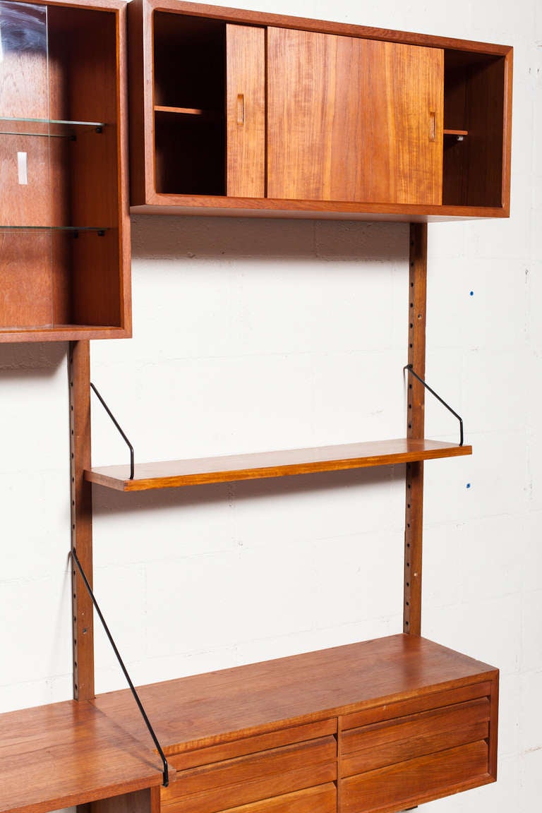 Three section teak wall unit with 2 sliding door cabinets, a curio cabinet, multiple shelves, a desk shelf flanked with drawer consoles. Original condition.