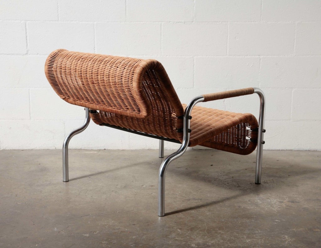 Low and Wide Wove Rattan Lounge Chair with Curved Tubular Crome Frame, and Rattan Wrapped Arm Rests.