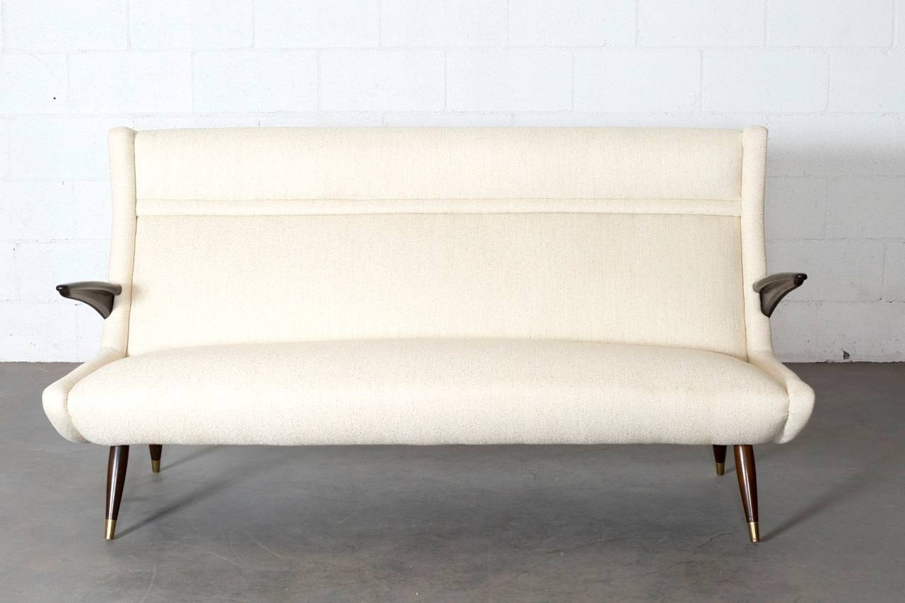 Mid-Century dark wood sofa with brass feet and new cream upholstery. Beautiful winged arms. Frame in original condition with some wear to brass feet consistent with age and use.