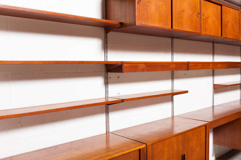 A four section storage unit by FM Mobler with 3 shelf lights. One light has broken plexiglass cover (see photo). Additional large cabinet storage space, large amount of shelf space, and a desk. This large teak unit embodies Scandinavian Mid-Century