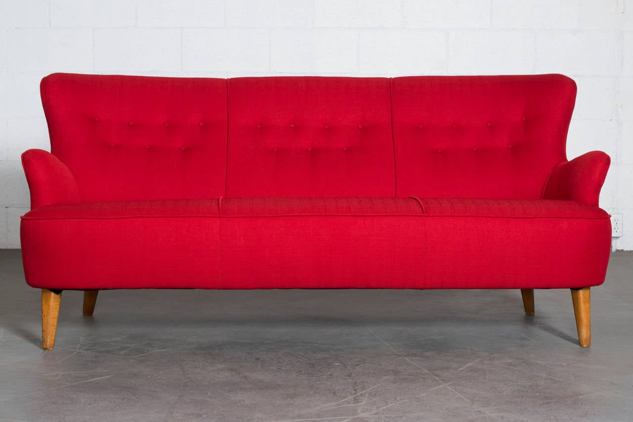 Adorable, curvy Theo Ruth three seater sofa with beechwood legs and new apple red upholstery. Legs have some signs of wear consistent with age and use.