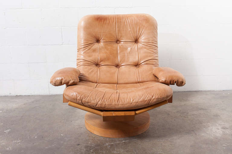 Solid oak swivel chair with natural leather cushion and matching ottoman. Unique system using leather pads for position adjustment. Some wear to wood frame consistent with age. Ottoman measures: 20 x 13.25 x 13.5.
