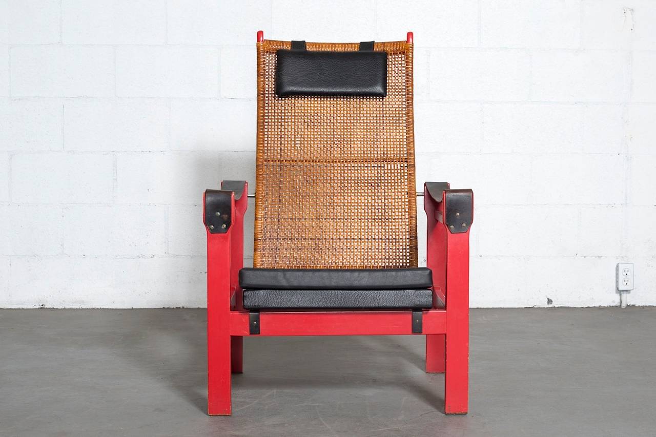 Lounge chair designed by P.J. Muntendam for Gebr. Jonkers. Beautifully woven rattan back and painted red wood frame with skai upholstered seat and headrest pillow. Worn black leather armrests. Institutional orange painted frame, 1970s production,