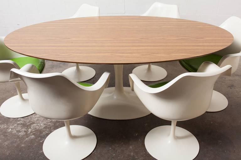 Iconic tulip dining set designed 1956,this example executed 1966 consists of a large oval dining table with faux-rosewood laminate top and six swivel armchairs with vinyl upholstery. Tulip bases are enameled aluminum, chair shells are lacquered