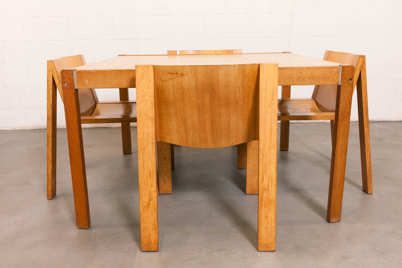 Finished Plywood Dining Set with Four Large Chairs and a Linear Seat Structure. Wear to Finish and Wood Consistent with Age and Use. Chairs measure 24 x 21.75 x 29.5