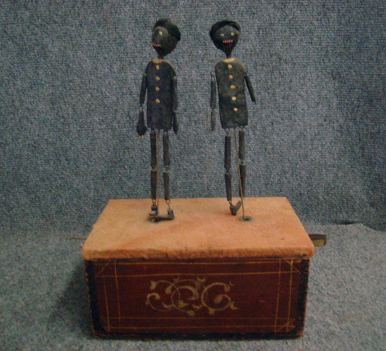 Folk art dancing toy, with two hand-made black dancers on a paint decorated wooden stand. The stand is decorated on all four sides. Circa 1880, American. 

Pull the wires on each side of the stand and watch the dancers do the jig. One of the