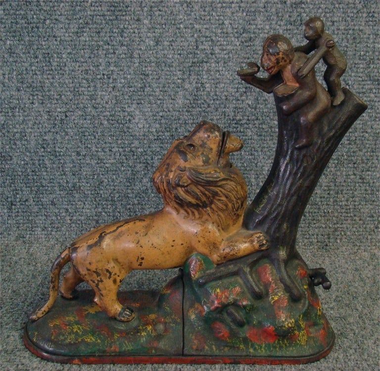 Kyser & Rex cast iron lion and two monkeys mechanical bank, with one tree knot shaped as a peanut. The lion has glass eyes. 

The bank is in good working order and has its original paint, which is somewhat worn due to age and usage. The cover on