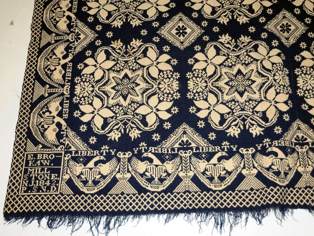 An exceptional center-seam coverlet, having a summer-winter weave in indigo and white. The field has repeating star and floral medallions. The border has emblematic eagles in tassel and swag borders, with LIBERTY woven forward and in reverse above