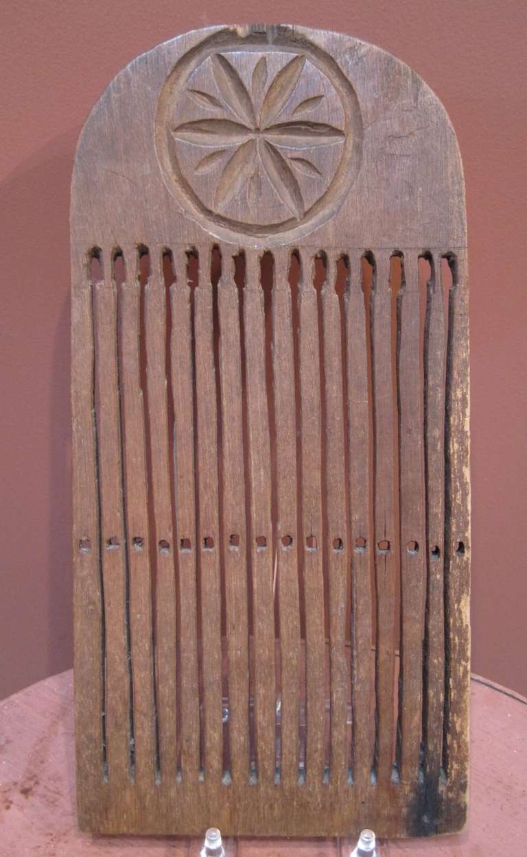 Early tape loom, birch, with a carved pinwheel decoration on one side and a partially completed pinwheel on the reverse. There is a small repair that was done early in its life, as evidenced by the hand-forged nail used. This tape loom dates from