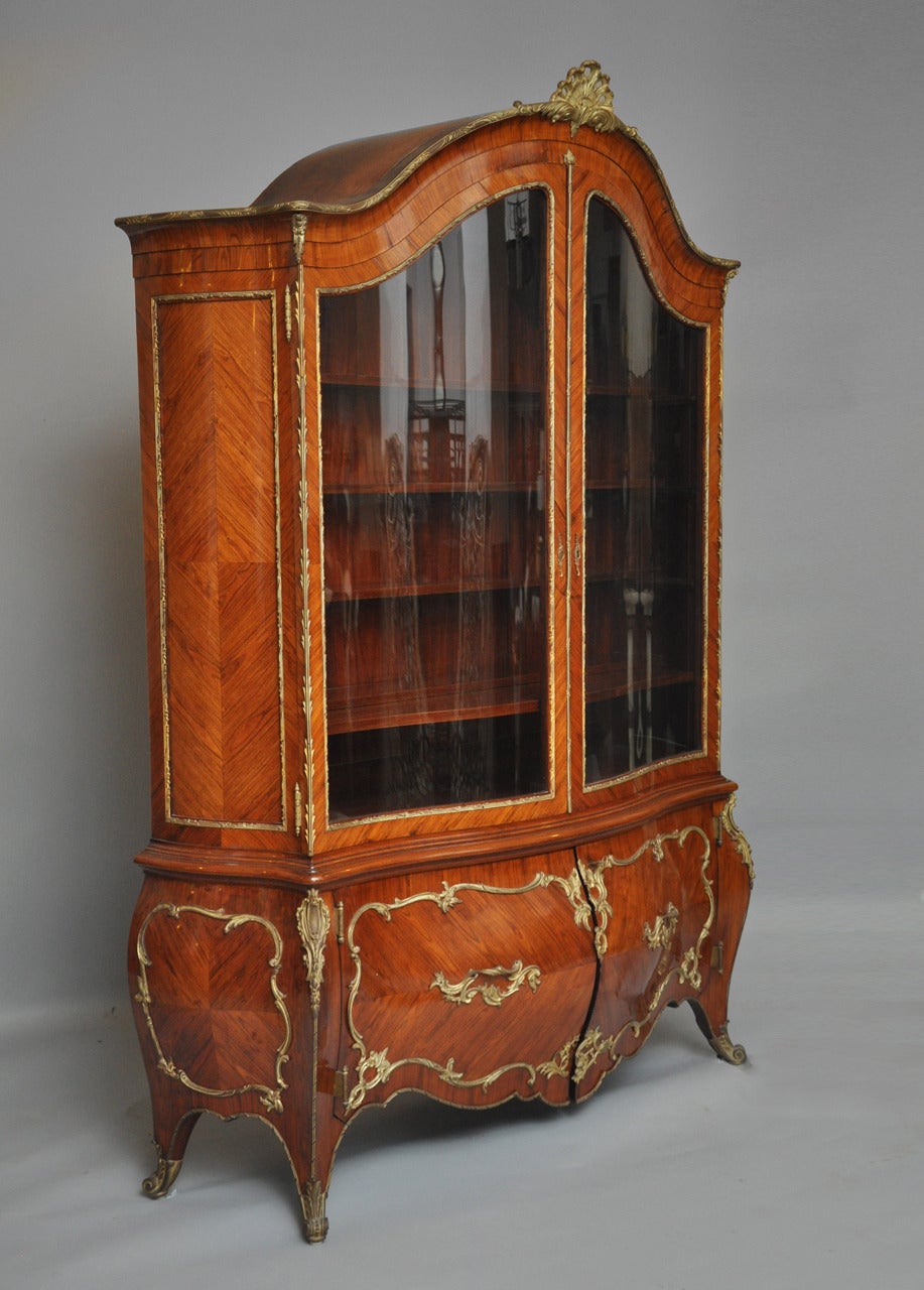 French Rococo Bombé Vitrine or Bookcase with an outstanding curvaceous shape which epitomizes the fine craftsmanship of the Rococo style. Bois De Violette “Kingwood” herringbone pattern frame with gilt bronze mounts, an arched bonnet surmounted with
