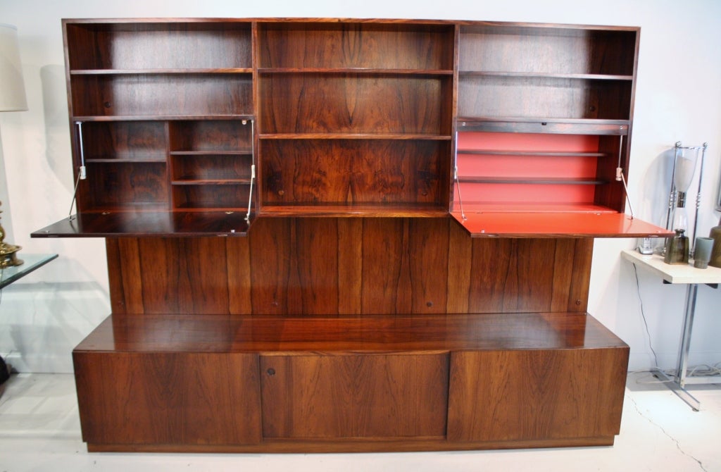 Stunning Danish modern rosewood wall unit storage system by Poul Cadovius.  This immaculate system features 3 assembled pieces including lower sideboard storage unit, a light up enclosed bar with bright red laminate interior, another storage