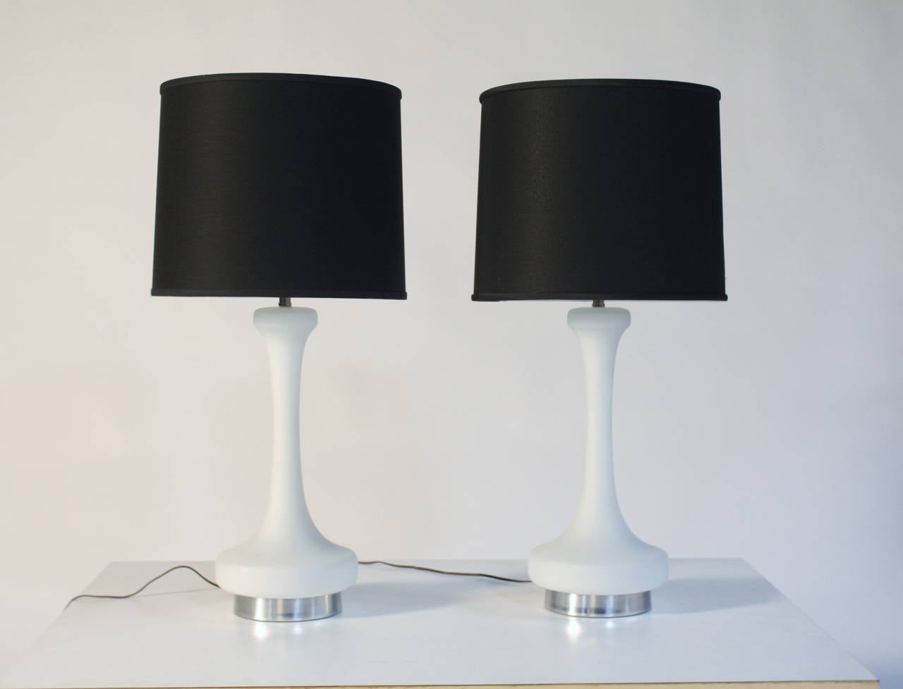 Elegant pair of 1970s white satin glass lamps with brushed chrome bases by Laurel.
Illuminates inside the base perfect for night light. New black shades measure 15
