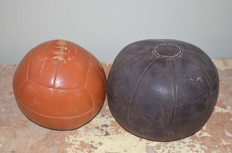 Pair of leather medicine balls from the 1930s display a rich contrast of color, size and tactility. The larger, 12