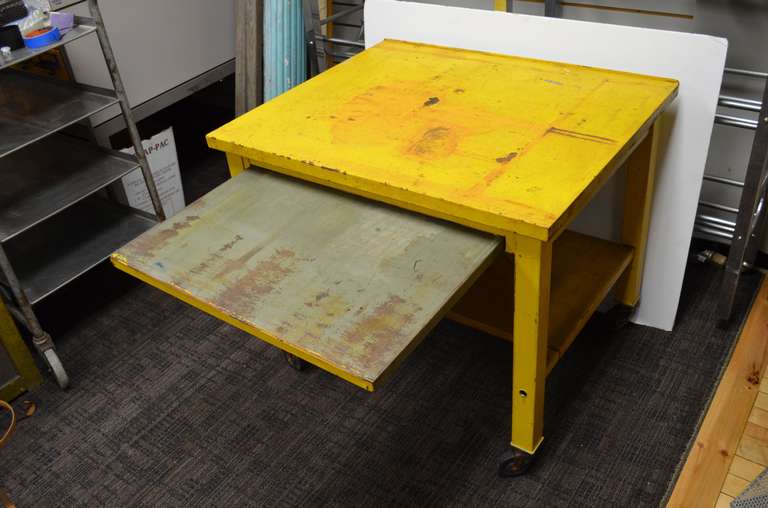 Steel industrial table on wheels with pullout and lower steel shelves. Here's a piece to brighten your day with its eye-catching sunshine yellow paint with orange highlights. Rolls around nicely for easy transport from patio to porch to hallway and