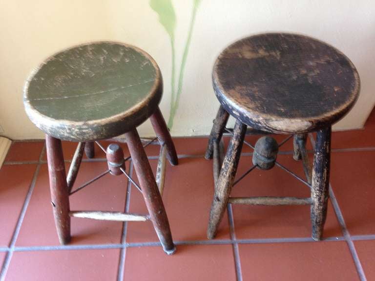 Classroom stools hailing from an early 20th century schoolhouse in Maine, early grades. One black, one green, rock-sturdy. Note the hand-turned, wooden dowel beneath each seat that acts as a hub for the additional metal bars running to the turned