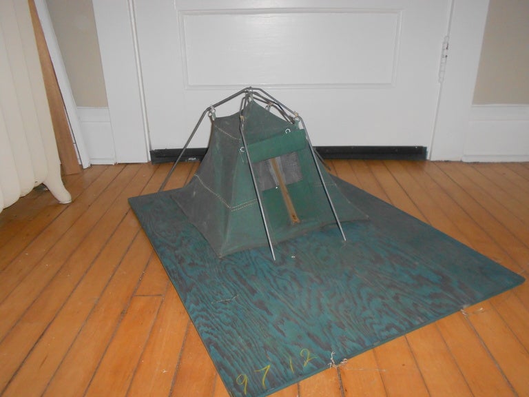 This Canvas Tent has been downsized to serve as a salesman's sample. Constructed of heavy-duty, water repellant canvas, accurate in every detail in miniature from zippered, screened entrance flap to steel support poles, mounted on a plywood platform