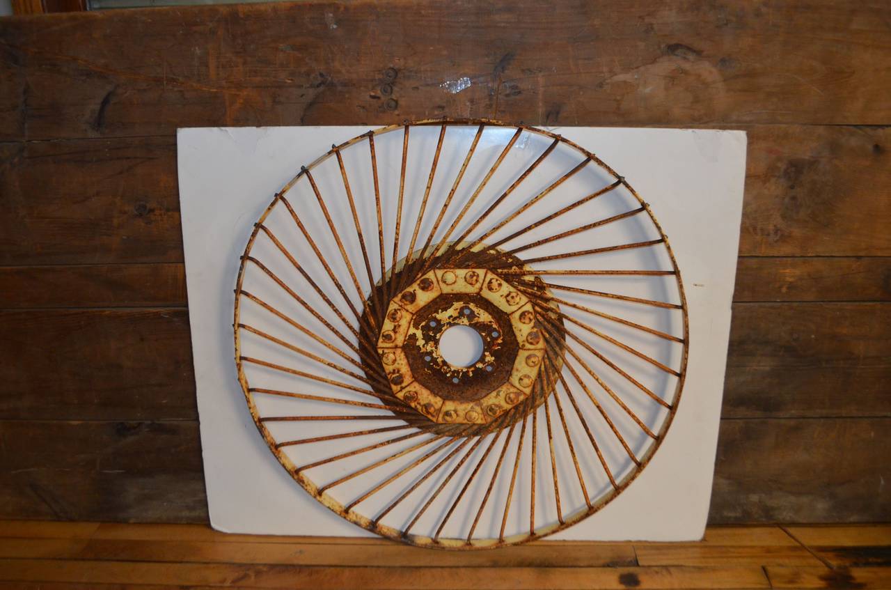 Vintage wheel from farm implement conveys lyrical motion as wall-mounted sculpture. Even stationary, this wheel appears to be spinning, projecting that  rapturous sense of coiled energy forever unwinding. Just love the patina of worn yellow paint