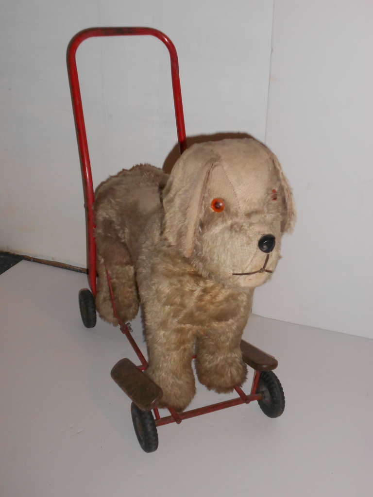 Antique child's toy dog could be ridden on its back or pushed like a stroller with its rubber wheels and red-painted handle. By the wear on its fur, this pup was obviously well loved. And who would wonder with a face like that. In fine working order
