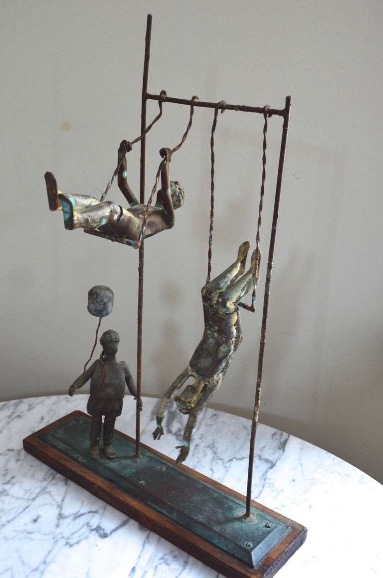 Sculpture in copper of three children at the playground.  Little girl with braids holds balloon as she watches her brothers(?) on the swings. Signed on the bottom of the wood base: L. Jensen, Playground Group No. 2. Mystique surrounds the provenance