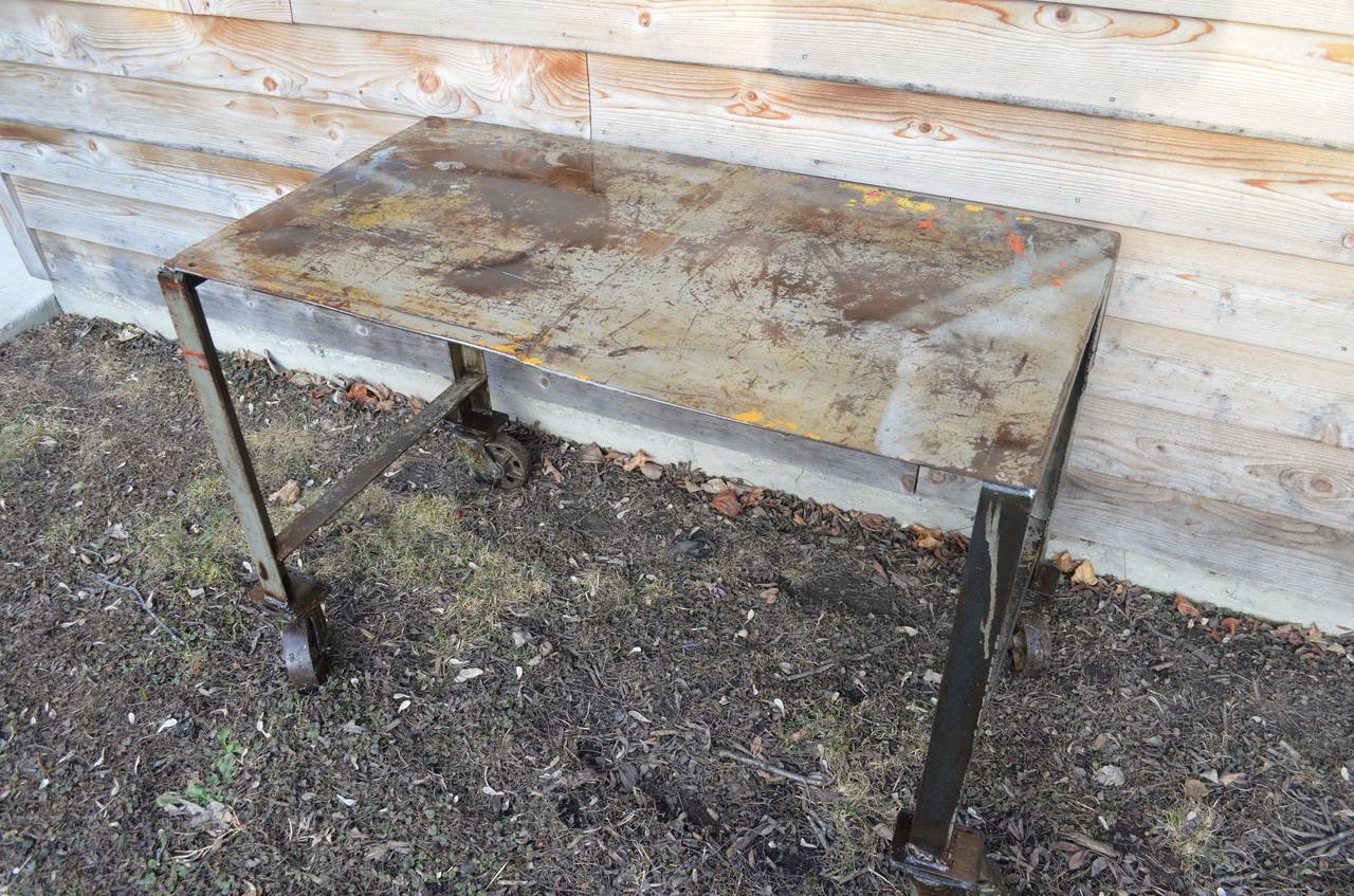 Factory table on pivoting steel wheels has been cleaned and sealed with spar urethane. We left the top in its as-found, working design of spilled paint, rusty patches, drips and scorches. A true working table of painterly beauty. Take a look at the