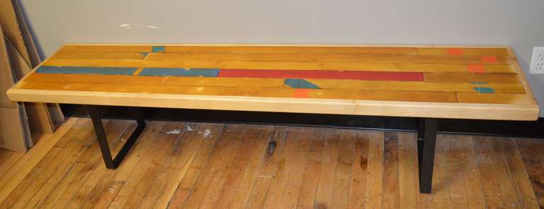 Gymnasium flooring salvaged from the demolition of a 100-year old high school has been made into a 6-foot long bench trimmed out in maple and sturdily mounted on steel leg brackets. The coloration is a random mix of the painted lines on the gym