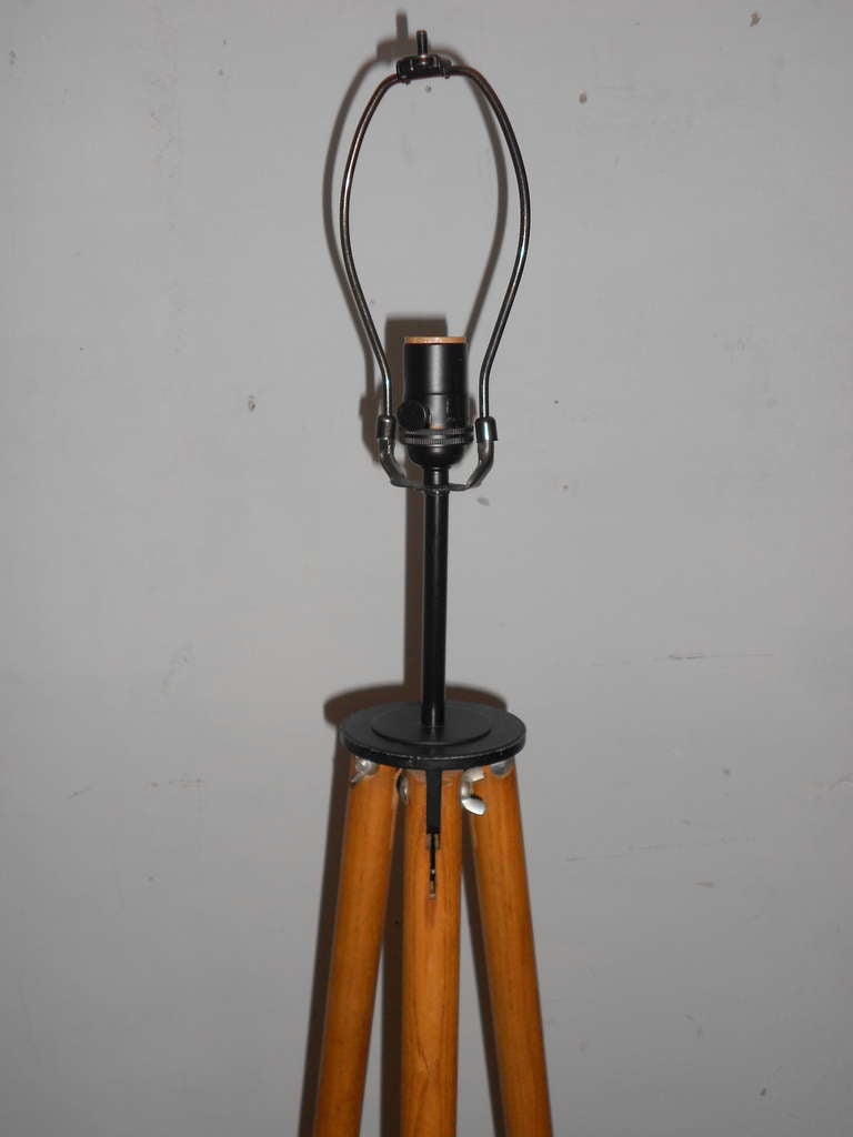 Surveyor's tripod has been transformed into a floor lamp with a simple, stately elegance. The round oak legs are tipped with black-painted steel feet. The lamp has been professionally wired with UL approved components, including 3-way black socket