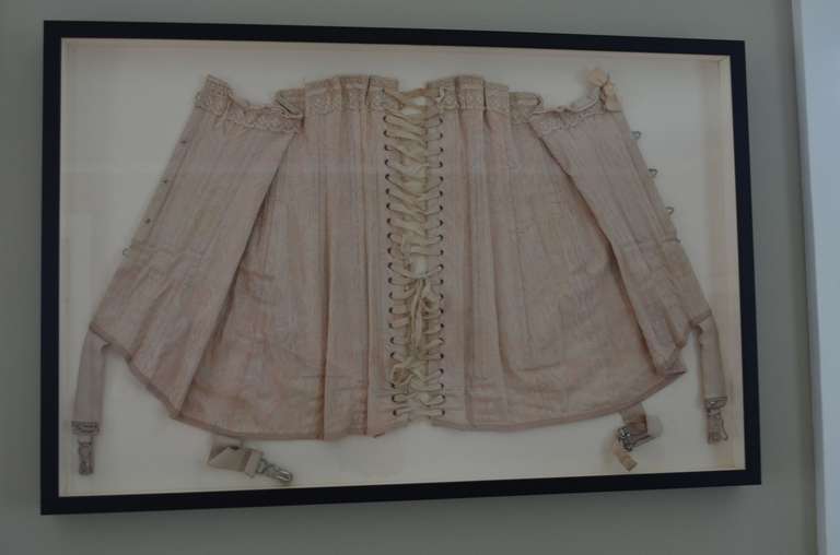 Victorian-era corset professionally framed in shadow box. Wonderfully detailed undergarment in soft pink silk embossed with a leaf pattern. Intricate lacing and garter straps complete this tactile foundation to the presentation of