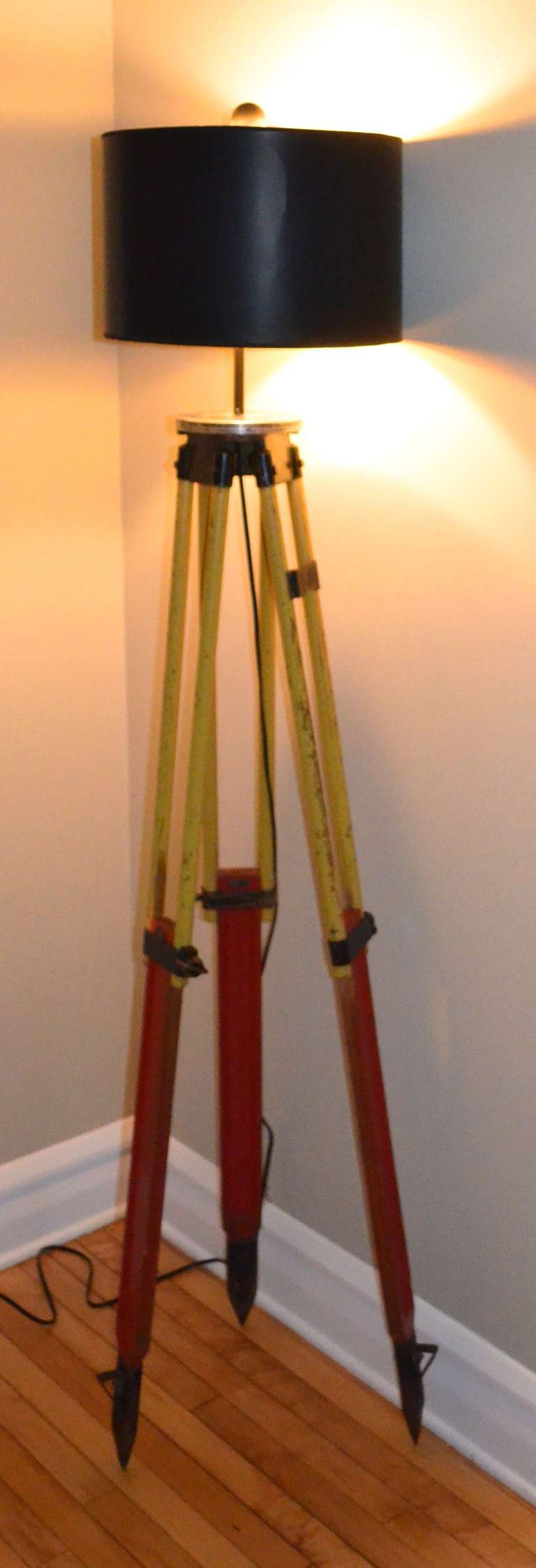 Surveyor's tripod as floor lamp. Professionally wired with UL-approved components including 3-way socket (max. 150 watts), 10-foot cord, harp and wooden ball finial painted black. Height adjusts from 48