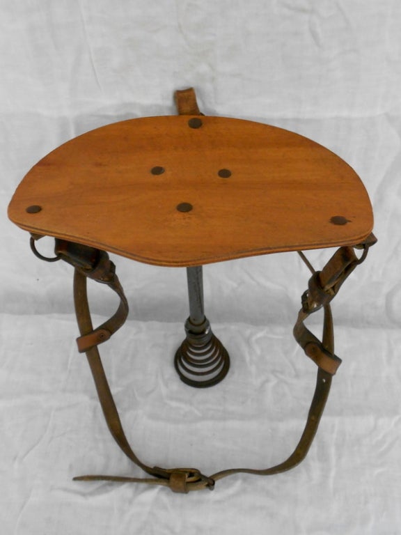Milking stool of wood and leather strapping with spring shaft on base. Farmer would strap stool to butt and move from cow to cow, using spring-loaded seat to sit alongside cow for milking. Saved wear and tear on the knees. Wonderfully sculptural