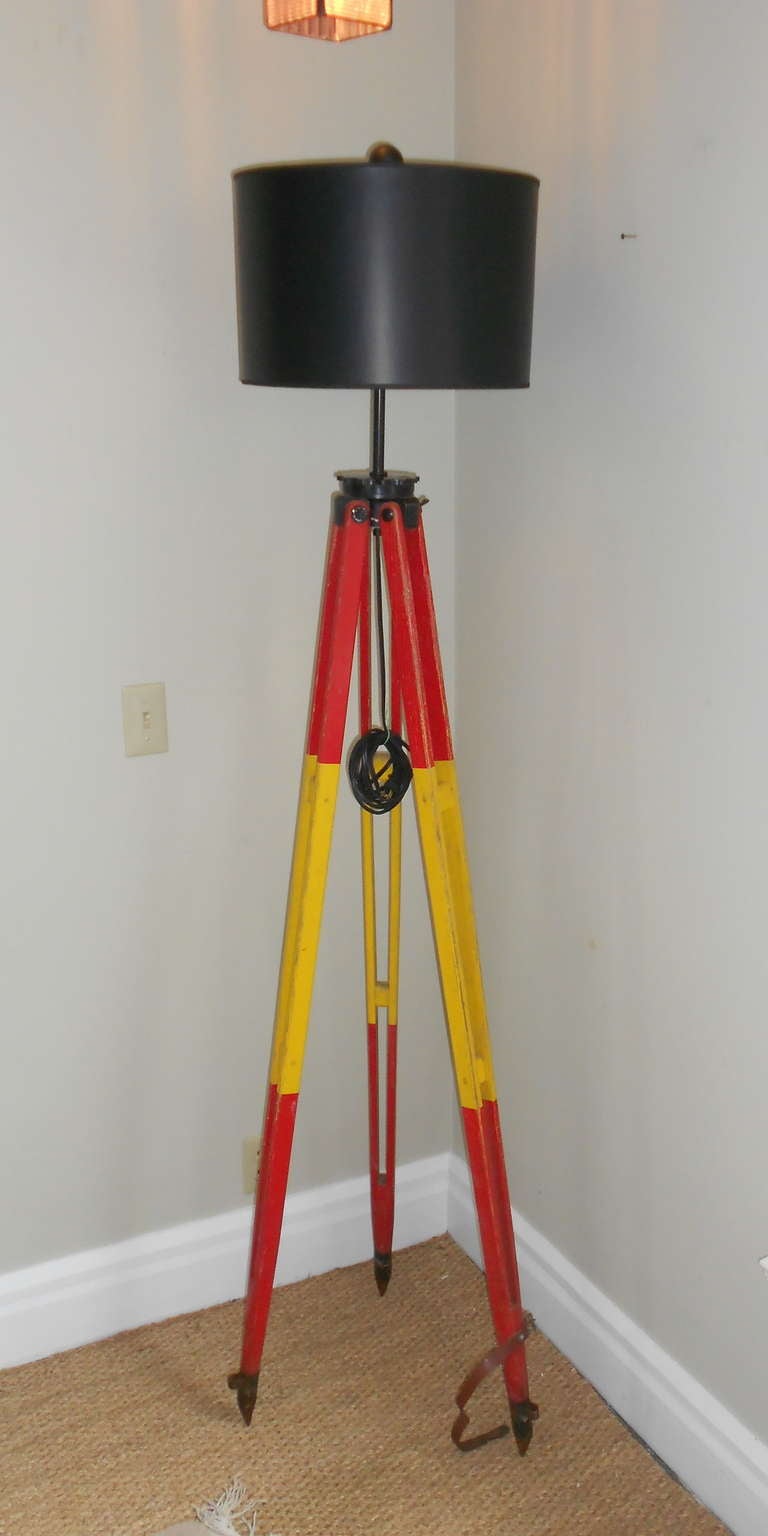 Wooden Surveyor's Tripod has been transformed into a floor lamp. The original paint on the wooden legs is a sharp red-yellow combo.  The legs are steel tipped with original leather strap attached for easy transport in the field. Lamp measures 75