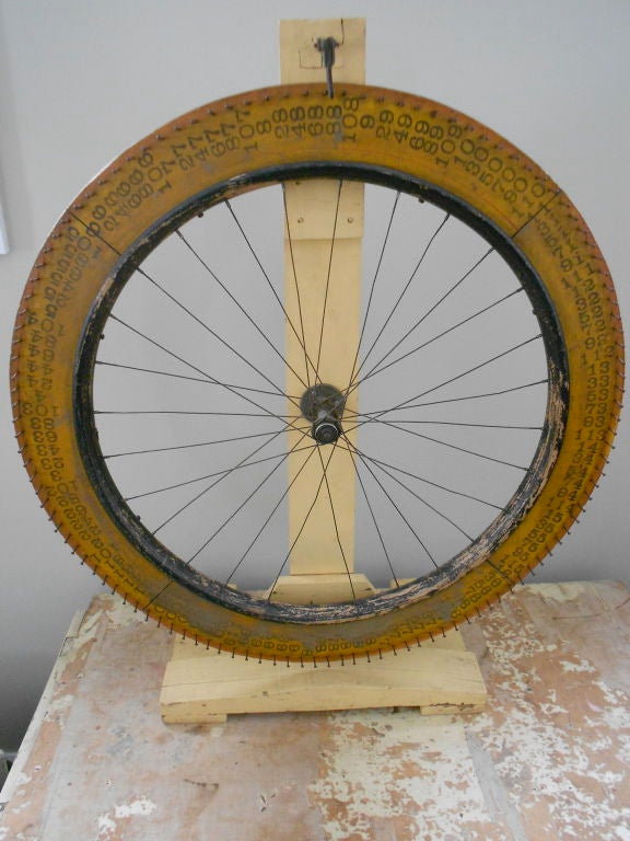 Early 20th century carnival wheel of fortune hand made from a wooden bicycle wheel. Mounted on a wooden stand, wheel spins to win, the clacking leather tongue coming to a stop on the winning number. In perfect working order, its orange, yellow and