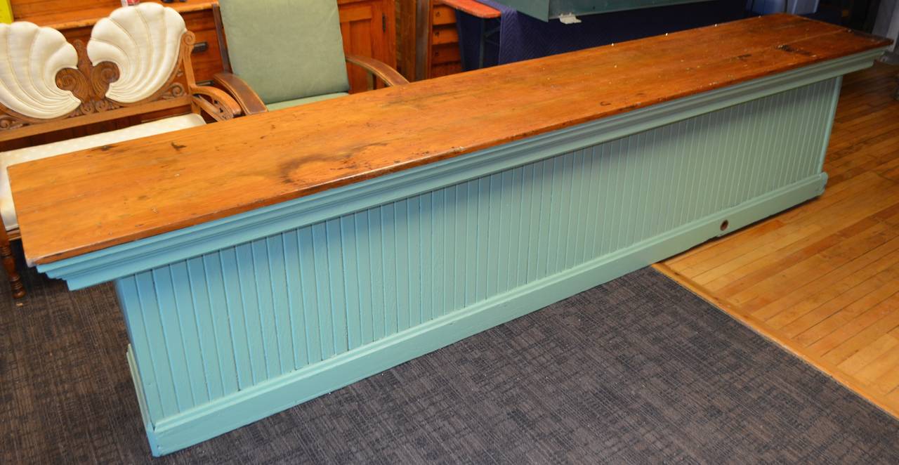 Store counter with three-board pine top and wainscoting facade with two shelves inside. Original paint. Light green on front, softer blue inside. A solid, substantial piece with significant scale and striking character. Measures: 10.5 feet long.