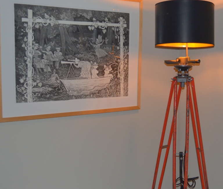 Steel, David White surveyor tripod in original orange color complete with sighting scope has been transformed into a statuesque floor lamp. Inclusion of the functioning, pivoting  scope adds an industrial/engineering dimension to the lamp,