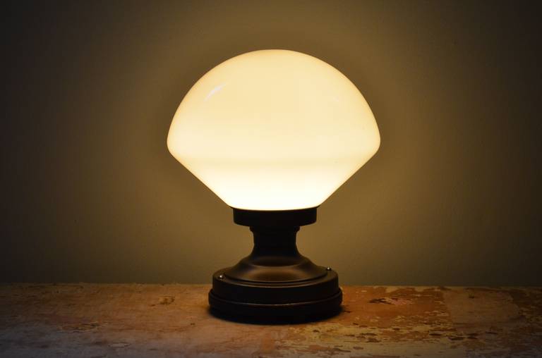 Milk glass, schoolhouse globe and steel fixture has been mounted on a wooden base to serve as a table lamp. Professionally wired with UL-approved components including porcelain socket and 8-foot black cord with inline switch. Casts a
