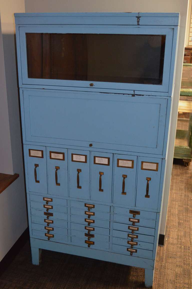 Early 20th century barrister cabinet provides significant storage and organizational capacity. Striking, as-found sky blue paint over steel with brass hardware/handles. Doors on top two units, glass front and solid, slide up and under. File drawers