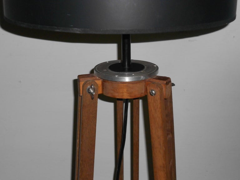 This wooden surveyor's tripod has been transformed into a floor lamp. The wooden legs appear to be walnut and have black steel tips. They are hinged midway for easy breakdown and transport in the field. The lamp has been professionally wired with