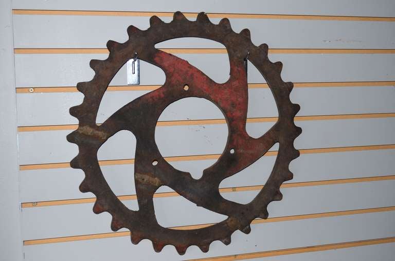 Cast iron gear from industrial machinery makes compelling wall art or garden ornamentation. Was painted red at one time by the look of the fading field of color. Not sure what kind of machinery this gear was a cog within but must have been sizable.