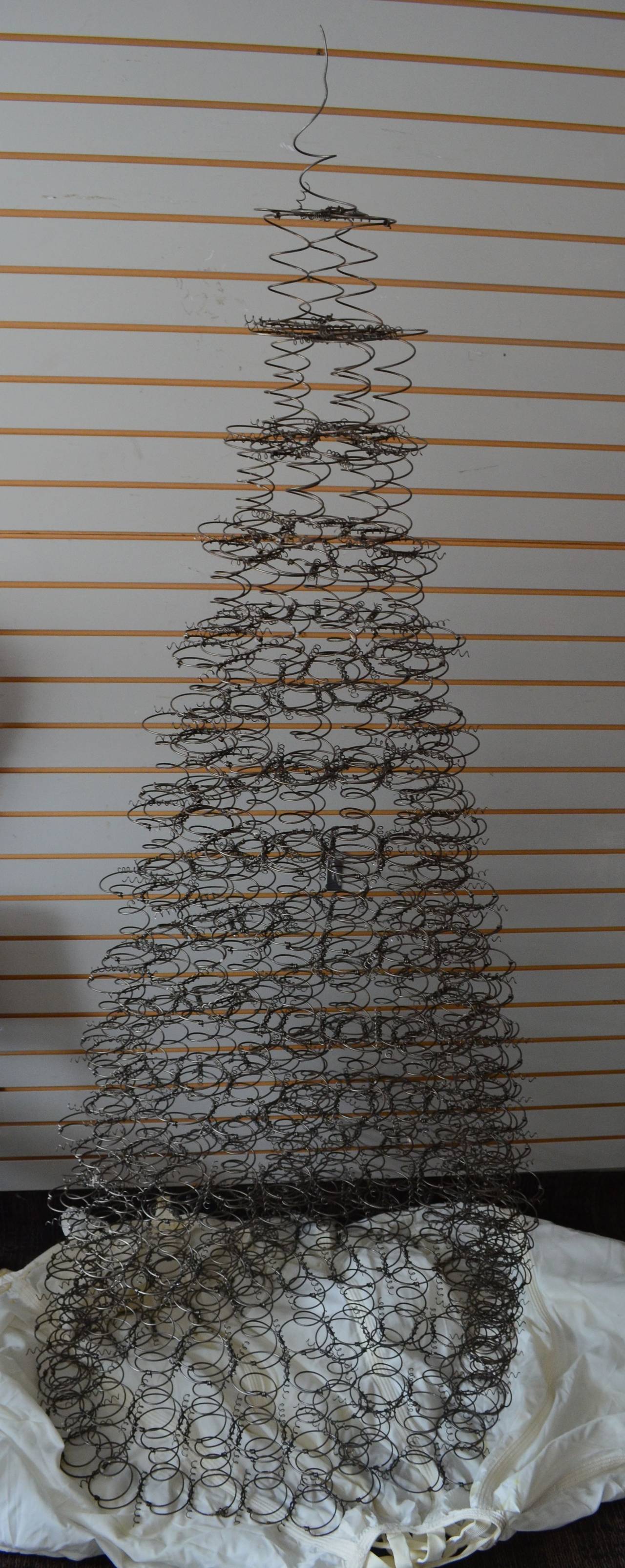 Mattress springs have been handwoven into a captivating, conical-shaped tree.  These steel springs were salvaged from vintage mattresses and have been intricately woven by hand into the shape of an evergreen tree. While this mattress spring tree