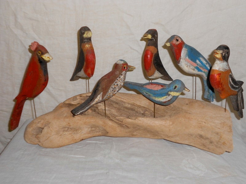 Set of seven songbirds, each mounted on metal rods drilled into driftwood stand. Birds are hand carved, hand painted and can be arranged in any configuration.