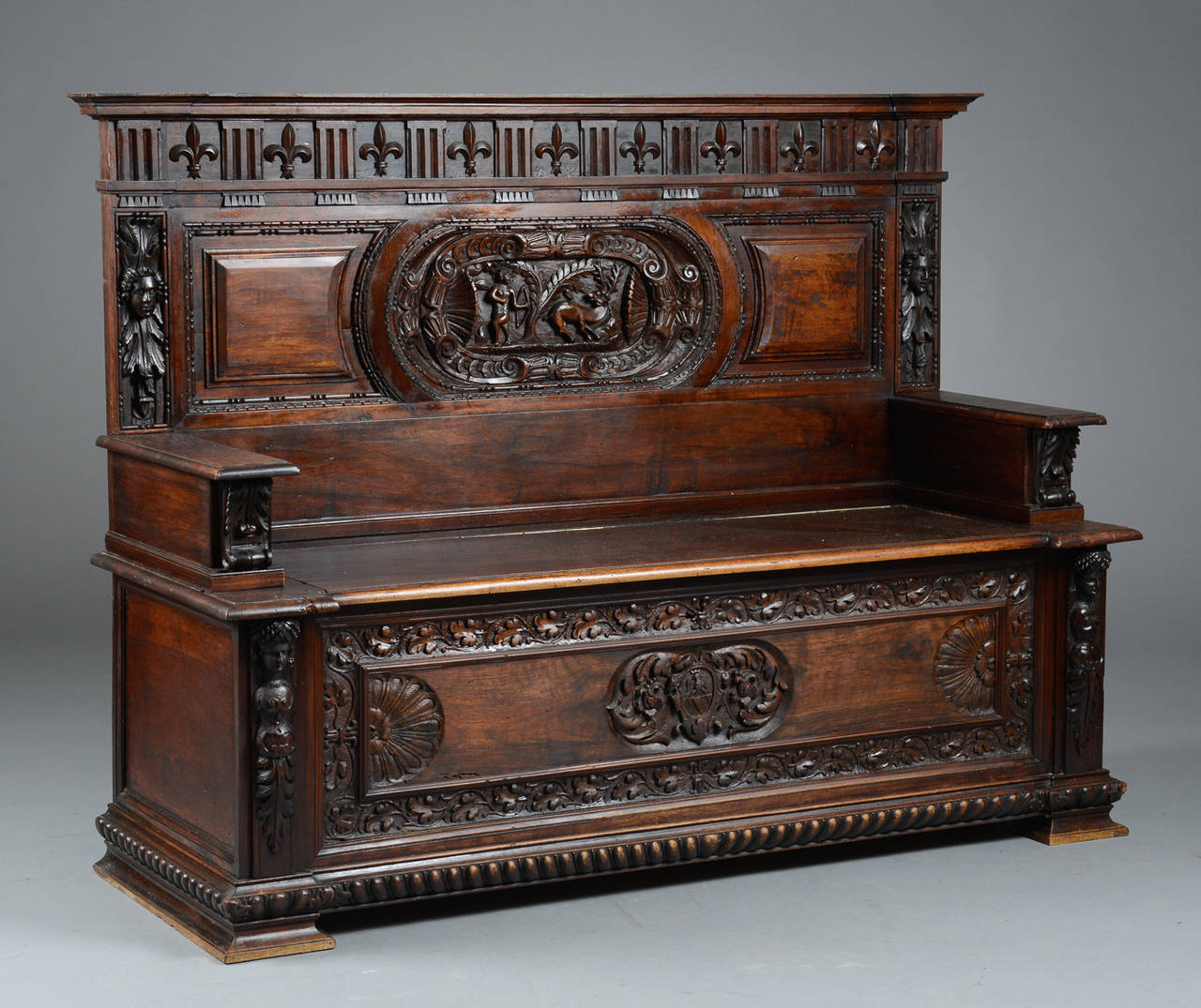 This highly ornate and carved walnut bench is from late 17th century Italy. The carved elements include the back with recessed landscape of Hermes and stag. The sides and lower front include elaborate carving and faces while fleur de lis crown the